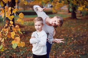 Happy girl and boy toss yellow autumn leaves in the forest photo