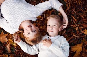 Happy girl and boy toss yellow autumn leaves in the forest photo