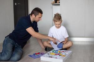 A cute boy in a white T-shirt collects an electrical designer with his dad in the room photo