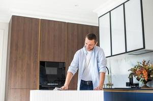 A man does wet cleaning in the kitchen, wiping the table with a napkin photo