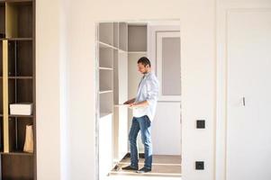 A man in a shirt stands in the apartment and collects shelves in the closet photo