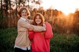 dos Adolescente muchachas son abrazando a puesta de sol y riendo foto