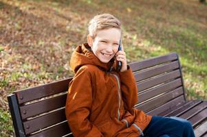 The boy is talking on the phone sitting on a bench and laughing photo