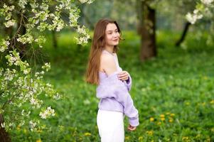 A young girl in a sweater next to white flowers on a tree photo