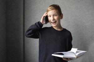 A happy boy is holding a book in his hands and talking on the phone photo