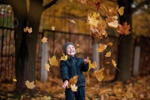 un chico en el otoño bosque lanza hojas y se regocija foto