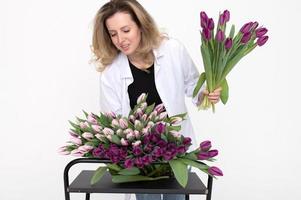 Cute florist girl in a shirt collects a bouquet of purple and white tulips for a birthday present photo