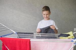 Cute boy hangs a wet towel on a metal clothes dryer, helps mom, housework, child's household chores photo