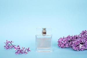 The perfume bottle stands on a blue background near the lilac flowers photo