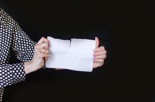 in women's hands, a white sheet of paper is almost torn into two parts. A field for text. Black background photo