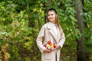 A cute girl with a red manicure with flowers in her coat pocket corrects the composition and smiles photo