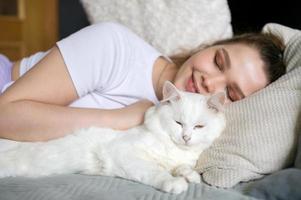 Cute girl sleeping on a bed next to a white cat photo