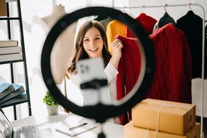 Fashion blogger concept, Young Asian women selling clothes on video streaming.Startup small business SME, using smartphone or tablet taking receive and checking photo