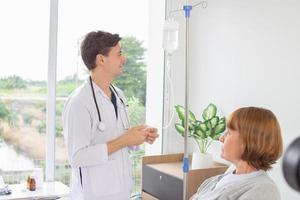 el médico es examinando el paciente en el hospital. caucásico médico vistiendo vestido y estetoscopio mirando a normal salina con un hembra paciente a el hospital. foto