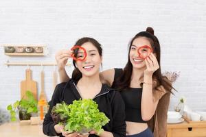 asiático activo dos mujer hermano en ropa de deporte disfrutar comiendo frutas sano alimentos hermosa chica, hermana participación campana pimienta, rebanado me gusta lentes. en el cocina. foto