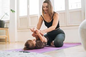 mujer joven en forma mamá con niña haciendo fitness en la alfombra en casa foto