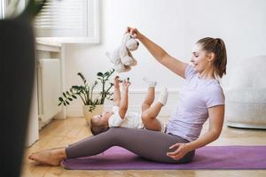 mujer joven en forma mamá con niña haciendo fitness en la alfombra en casa foto