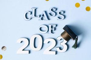 Class of 2023 concept. Wooden number 2023 with graduated cap on blue background with tinsel top view photo