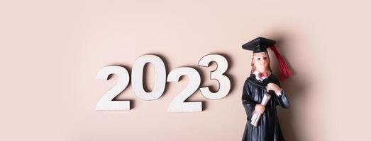 Class of 2023 concept. Wooden number 2023 with graduate statuette on beige background photo