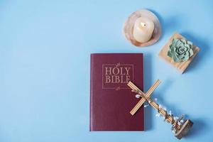 Christian Holy Bible with cross and candle on blue background, flat lay, top view photo