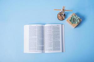 Open Holy Bible with cross and decorative flowers on blue background. Flat lay photo