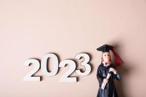 Class of 2023 concept. Wooden number 2023 with graduate statuette on color background photo