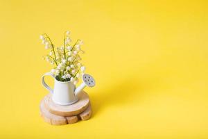 Lilies of the valley bouquet in a decorative watering can on a yellow background with copy space photo