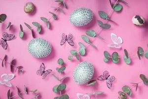 Pattern of Easter eggs, eucalyptus, butterflies and beads. Trendy flat lay composition on color background photo