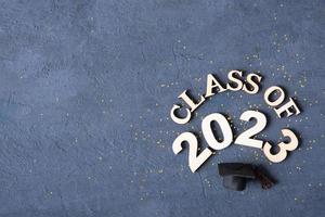 Class of 2023 concept. Wooden number 2023 with graduate statuette on concrete background with tinsel top view photo