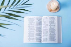 Open Holy Bible with candles and palm leaves on blue background photo