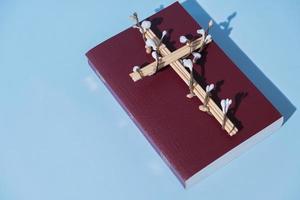cruz flores decoradas con la santa biblia sobre fondo azul. concepto minimalista de vacaciones de semana santa foto