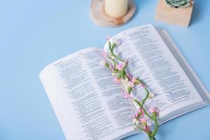 Christian Holy Bible with decorative flowers on blue background top view, flat lay photo