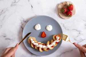 pequeños panqueques con fresas en la porción original en forma de cara sonriente. vista superior. endecha plana foto