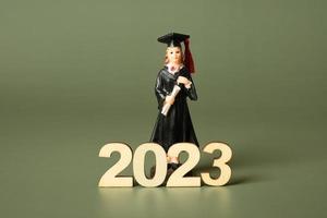 Class of 2023 concept. Wooden number 2023 with graduate statuette on color background photo