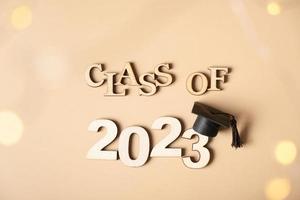 Class of 2023 concept. Wooden number 2023 with graduated cap on beige background with bokeh photo