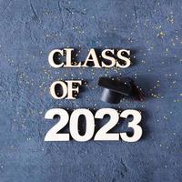 Class of 2023 concept. Wooden number 2023 with graduated cap on dark concrete background with tinsel photo