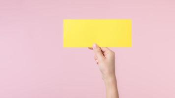 Woman hand holding and showing blank space paper for advertisement information message poster isolated on pink pastel studio background. photo