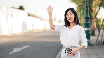 retrato joven hermosa asiático mujer ondulación mano a amigo por el calle en soleado día festivo. foto