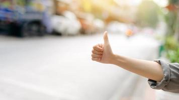 sonriente joven asiático mujer viajero autoestop en un la carretera en el ciudad. vida es un viaje concepto. foto