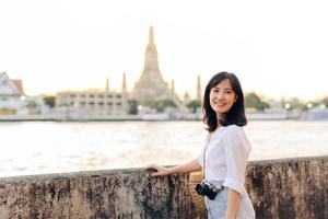 retrato joven hermosa asiático mujer sonriente mientras viaje a wat arun puesta de sol ver punto, bangkok, tailandia foto