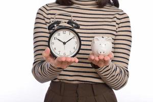 Portrait of young Asian woman casual uniform holding white piggy bank and alarm clock isolated on white background, Financial and bank saving money concept photo