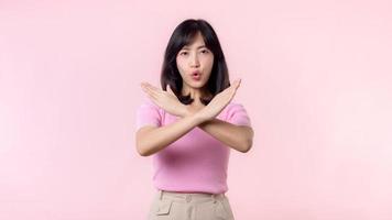 portrait serious young asian woman with cross arm gesture showing stop, no, wrong, denial, rejection sign isolated on pink pastel studio background. deny and negative expression symbol concept. photo