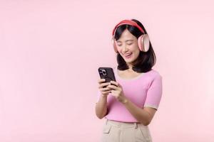 retrato alegre joven asiático mujer disfrutar escuchando audio por teléfono inteligente música solicitud en contra rosado. contento sonriente hembra persona con auricular. sonido, ocio, estilo de vida, tecnología concepto foto