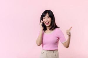 Pretty young asian woman showing success, victory hand gesture while receiving great news from smartphone on pink background. Happy technology, mobile phone advertisement, online application concept photo