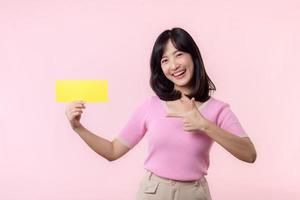 Portrait happy young woman model holding and showing blank space paper for advertisement information message poster with thumb up or point finger gesture isolated on pink pastel studio background. photo