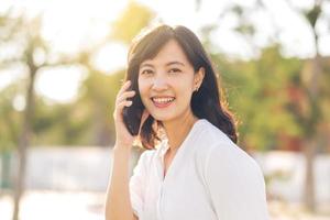 Portrait beautiful young asian woman with smart mobile phone around outdoor nature view in a sunny summer day photo