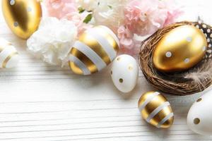 nido con Pascua de Resurrección huevos pintado dorado colores en un blanco de madera antecedentes. foto