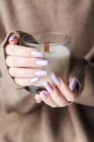 The hands of a young girl with a beautiful light purple manicure hold a candle photo