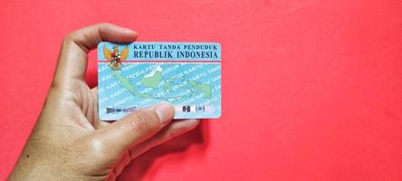 Man holding Indonesian citizen identity card, isolated on a red background and negative space. photo