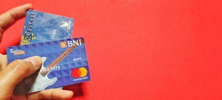 Man holding a bank savings card in Indonesia, isolated on a red background and negative space. photo